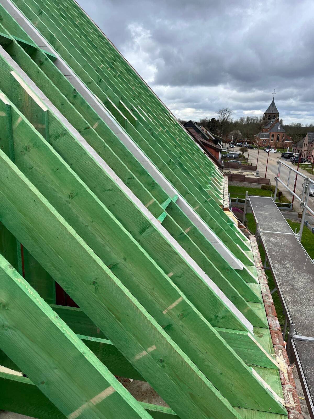 Houten dakspanten van een nieuw hellend dak met uitzicht op een kerk.