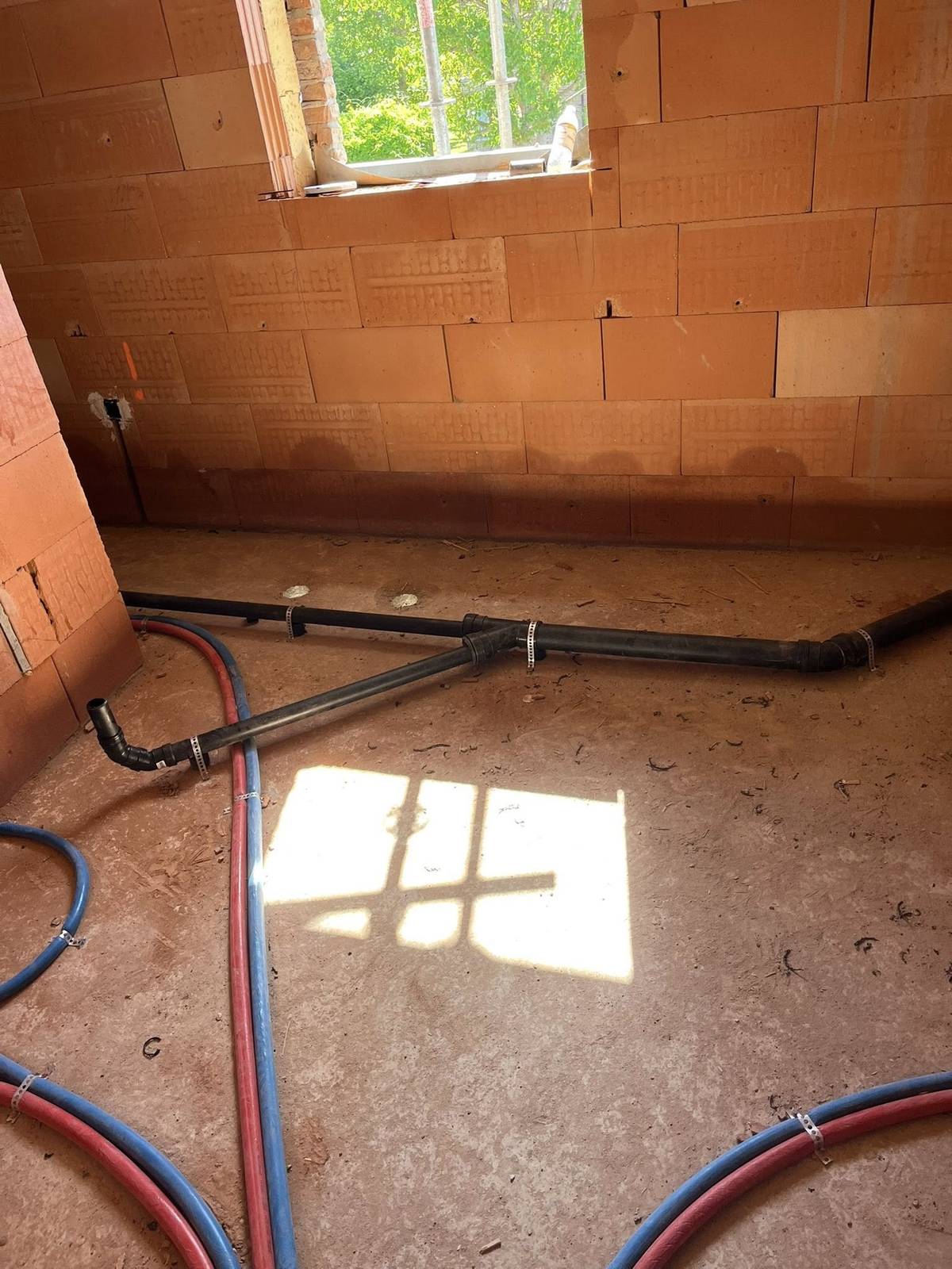 Afvoerleidingen en waterleidingen op een betonnen vloer in een onafgewerkte ruimte.