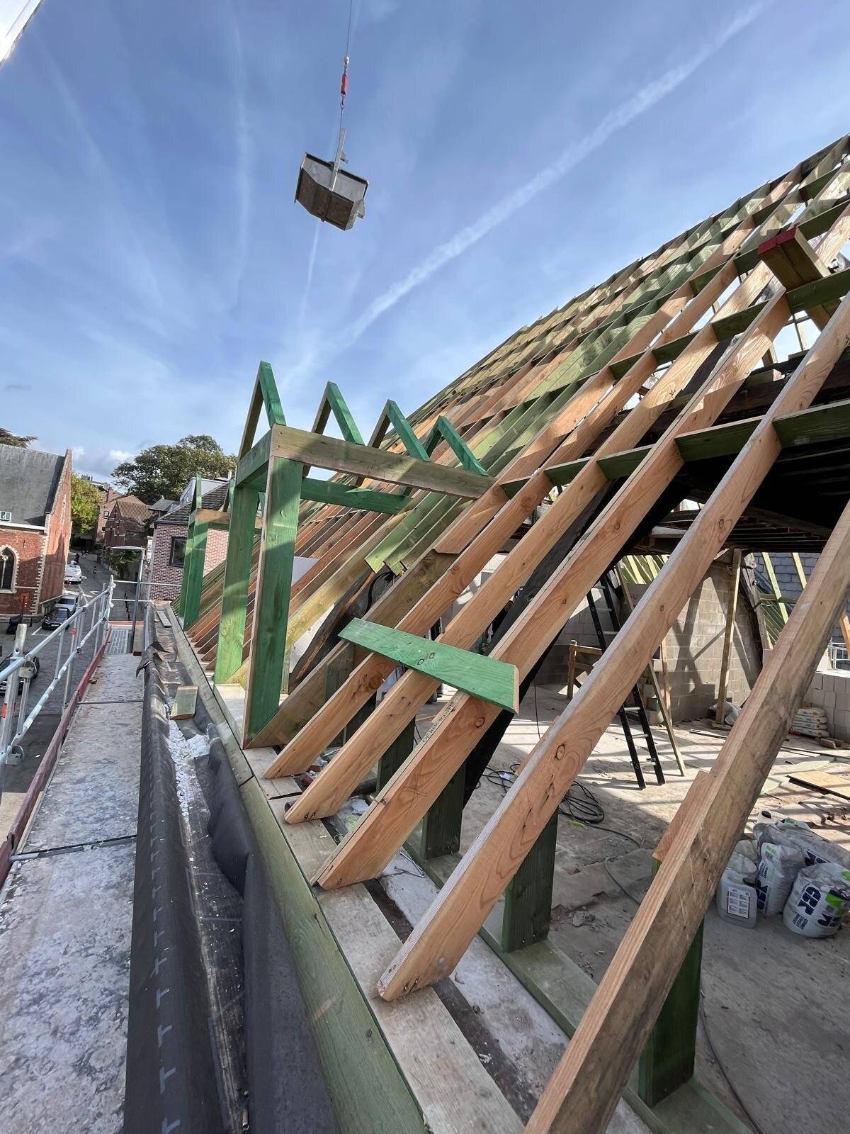 Nieuwe houten dakconstructie van een hellend dak met materialen die door een kraan worden aangeleverd.