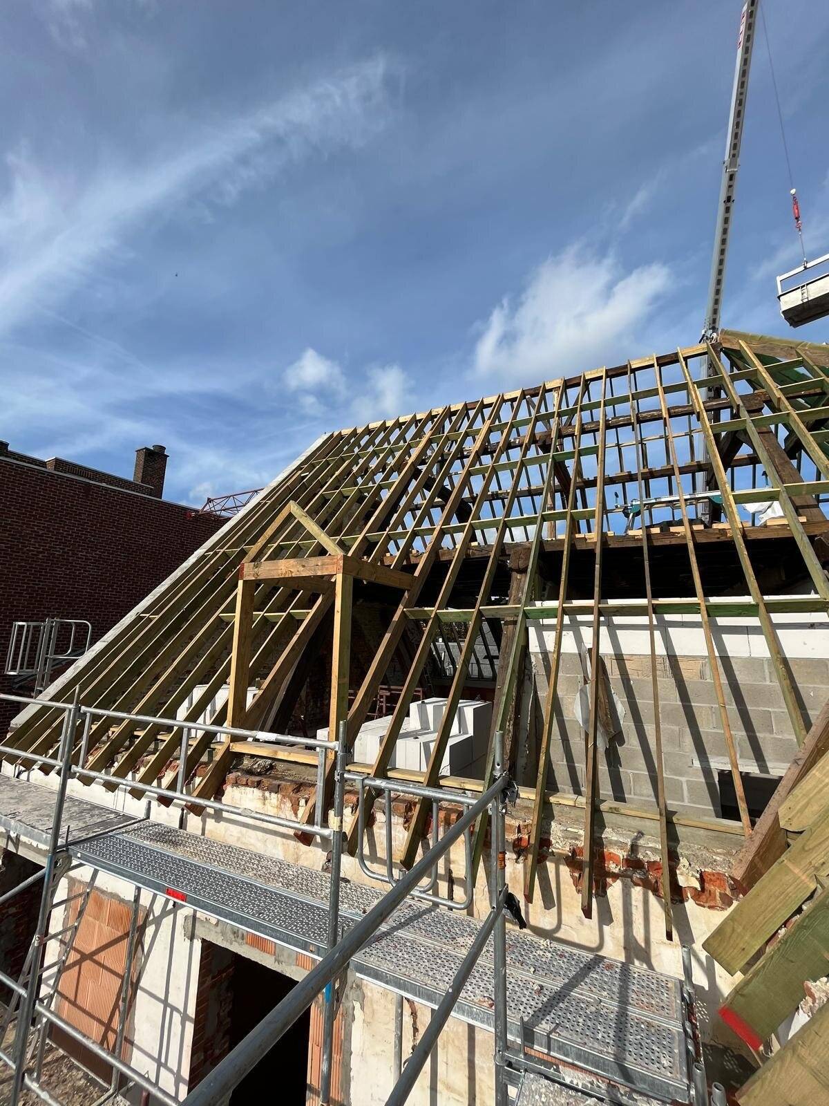 Nieuwe houten dakconstructie van een hellend dak met dakkapel in aanbouw, omgeven door steigers.