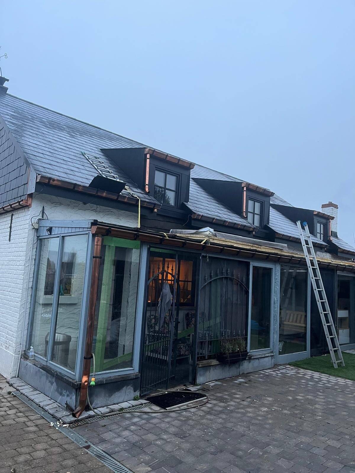 Huis met deels vernieuwd pannendak en een ladder, bij zonsondergang.