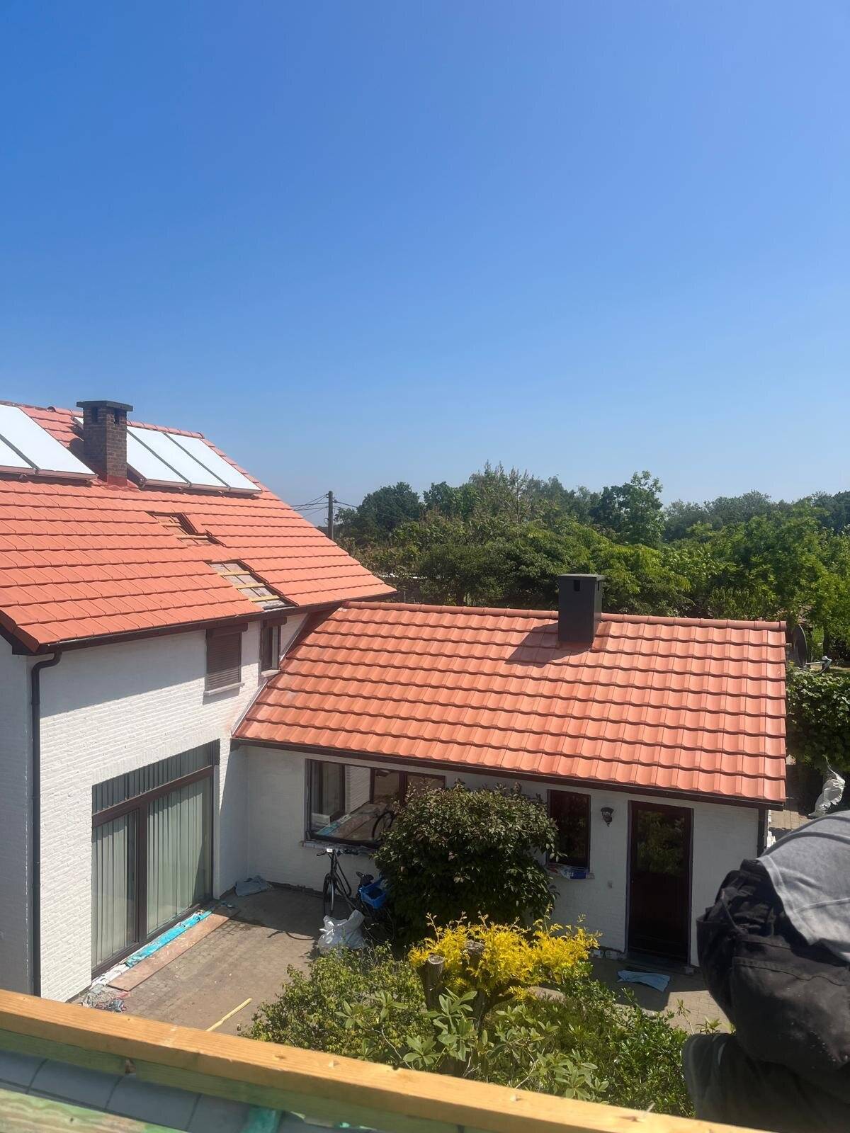 Overzicht van een huis met een nieuw hellend dak van rode dakpannen, een aanbouw, en zonnepanelen op het hoofddak.