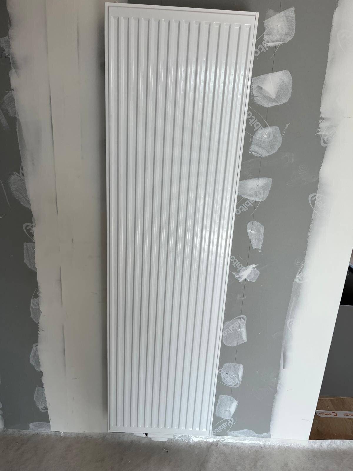 Nieuwe witte verticale radiator gemonteerd tegen een muur die voorbereid wordt voor afwerking.
