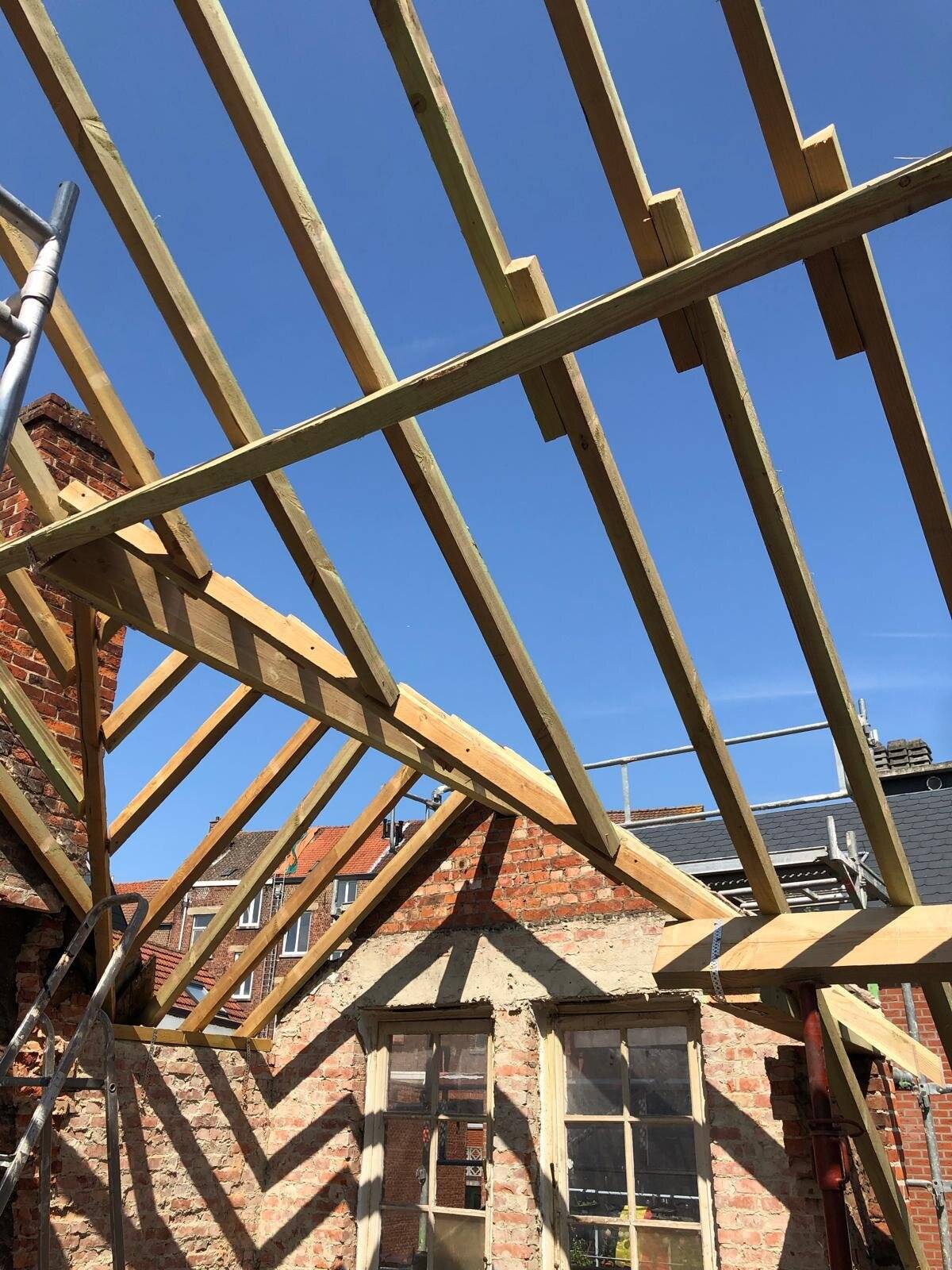 Houten dakconstructie van een hellend dak onder een blauwe lucht.