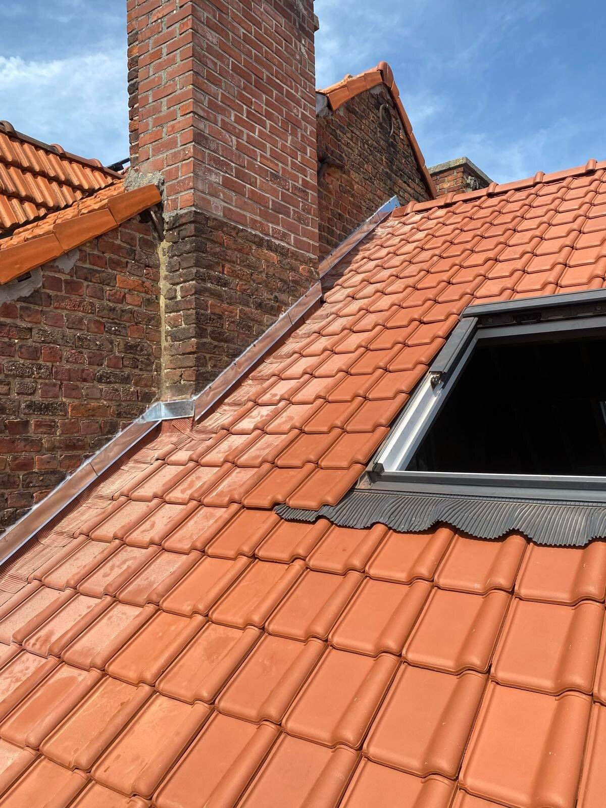 Nieuw dak met rode dakpannen, Velux dakraam en een bakstenen schoorsteen