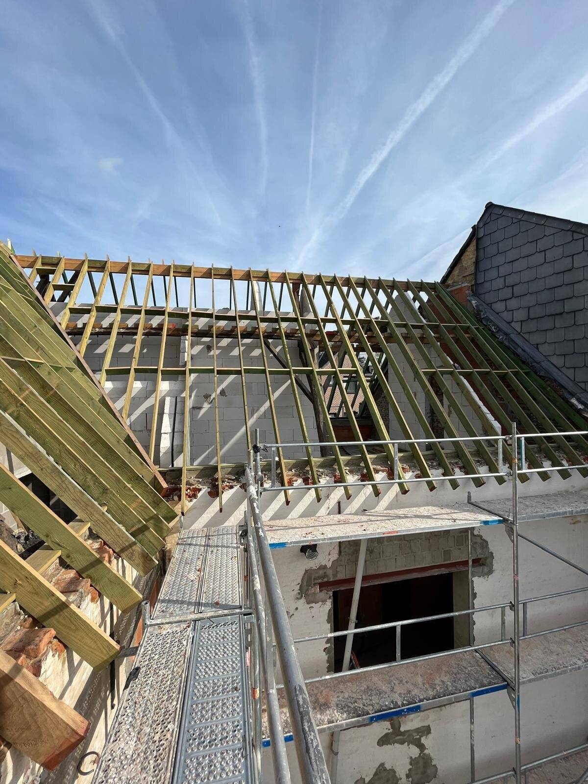 Nieuw hellend dak in opbouw met zicht op de houten dakconstructie en stellingen.