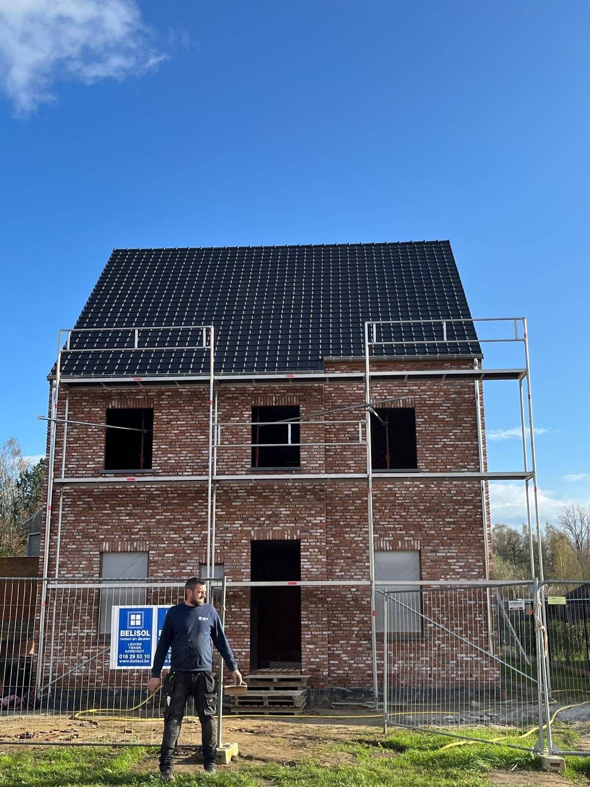 Teamlid staat voor een nieuwbouwhuis met afgewerkt hellend dak en steiger.