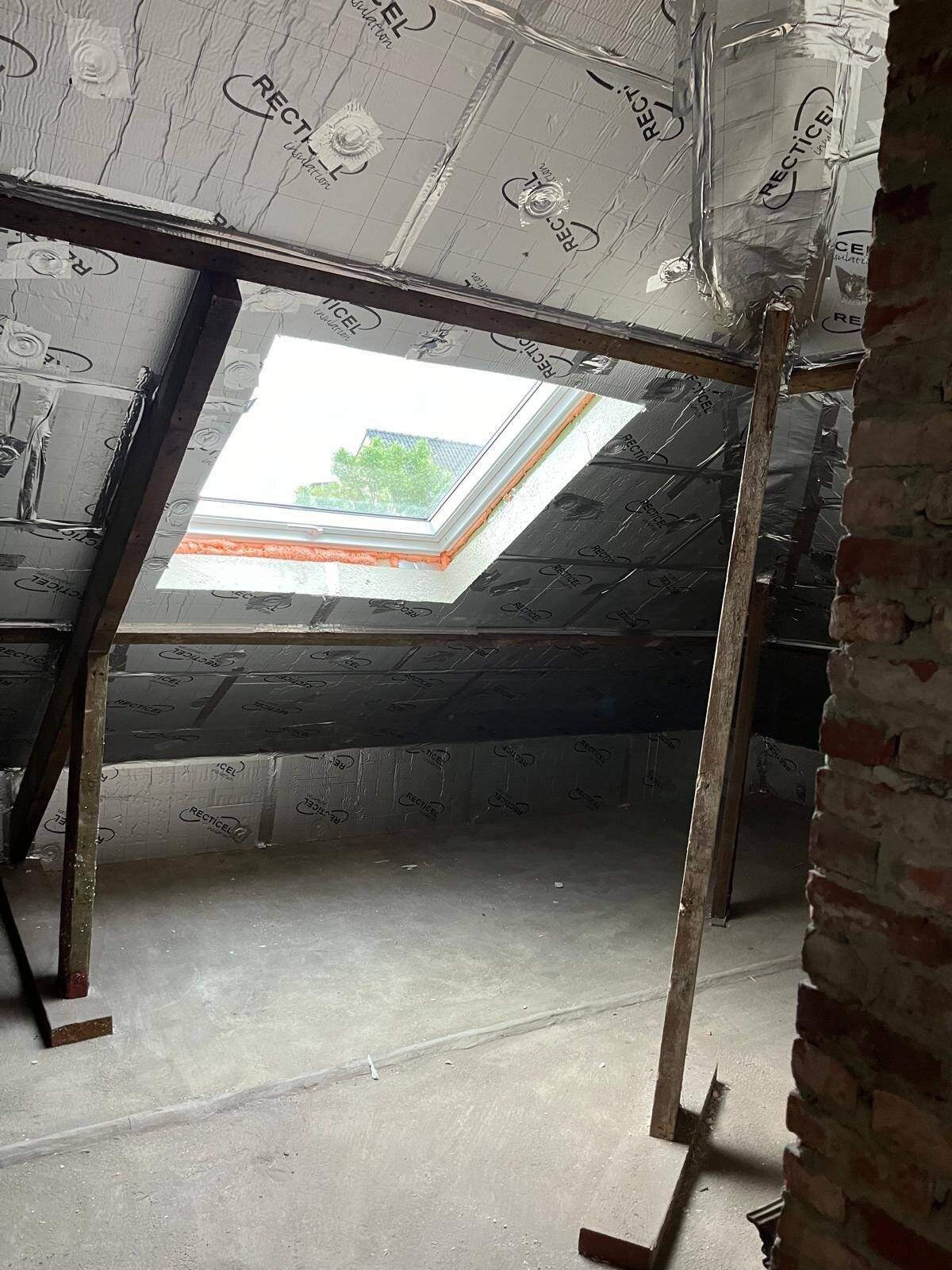 Binnenzicht van een hellend dak met geïnstalleerde Velux en isolatieplaten.