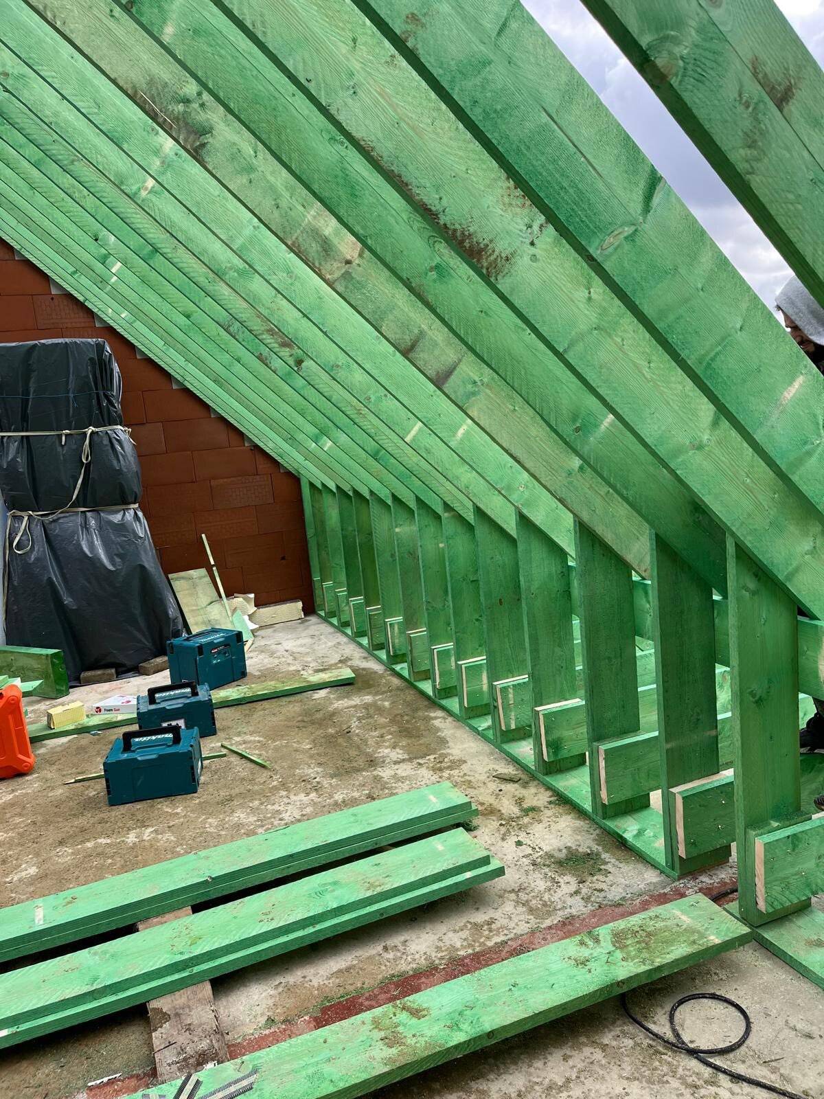 Interieur van een nieuwbouwdak met groene houten spanten en bouwmaterialen op de grond.