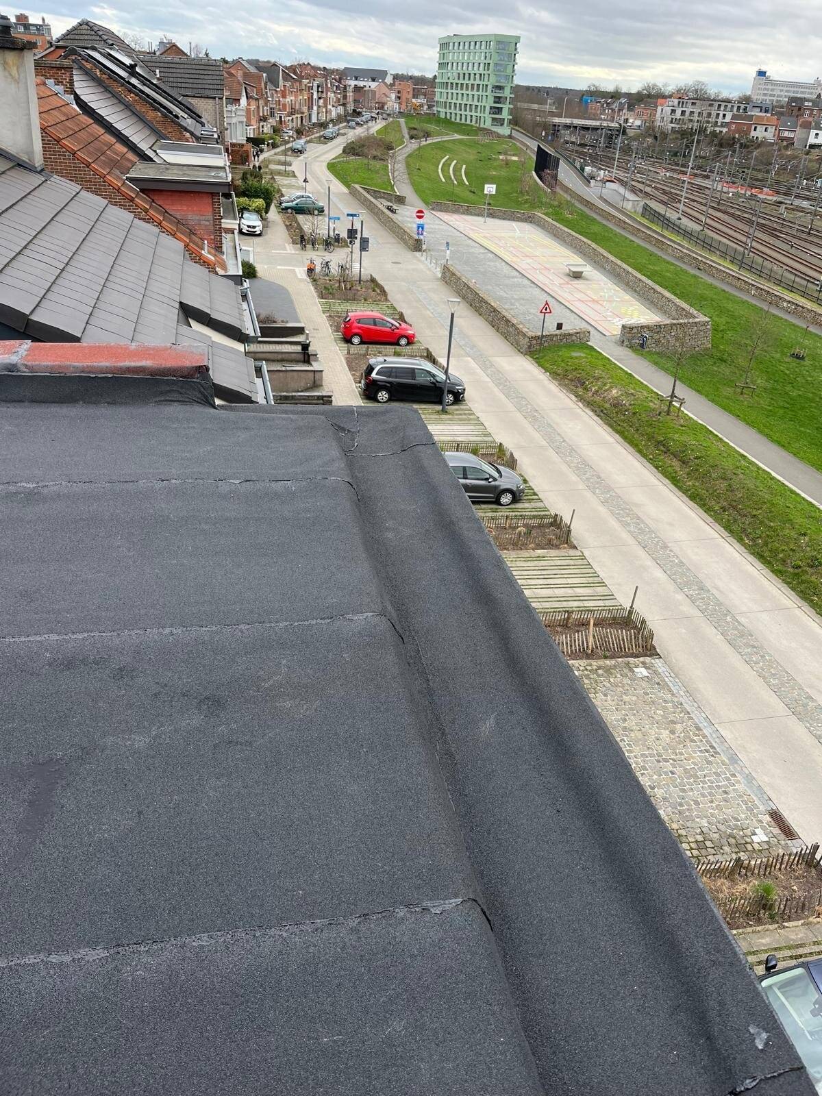 Panoramisch uitzicht vanaf een plat dak over een weg en stedelijke bebouwing.
