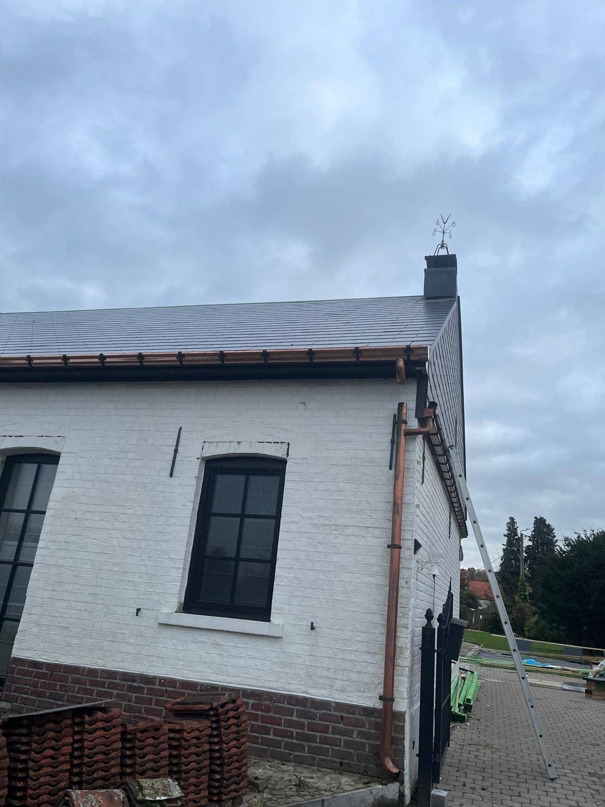 Gerenoveerd wit huis met nieuw hellend dak, koperen dakgoten en regenpijpen, en een schoorsteen met windvaan.