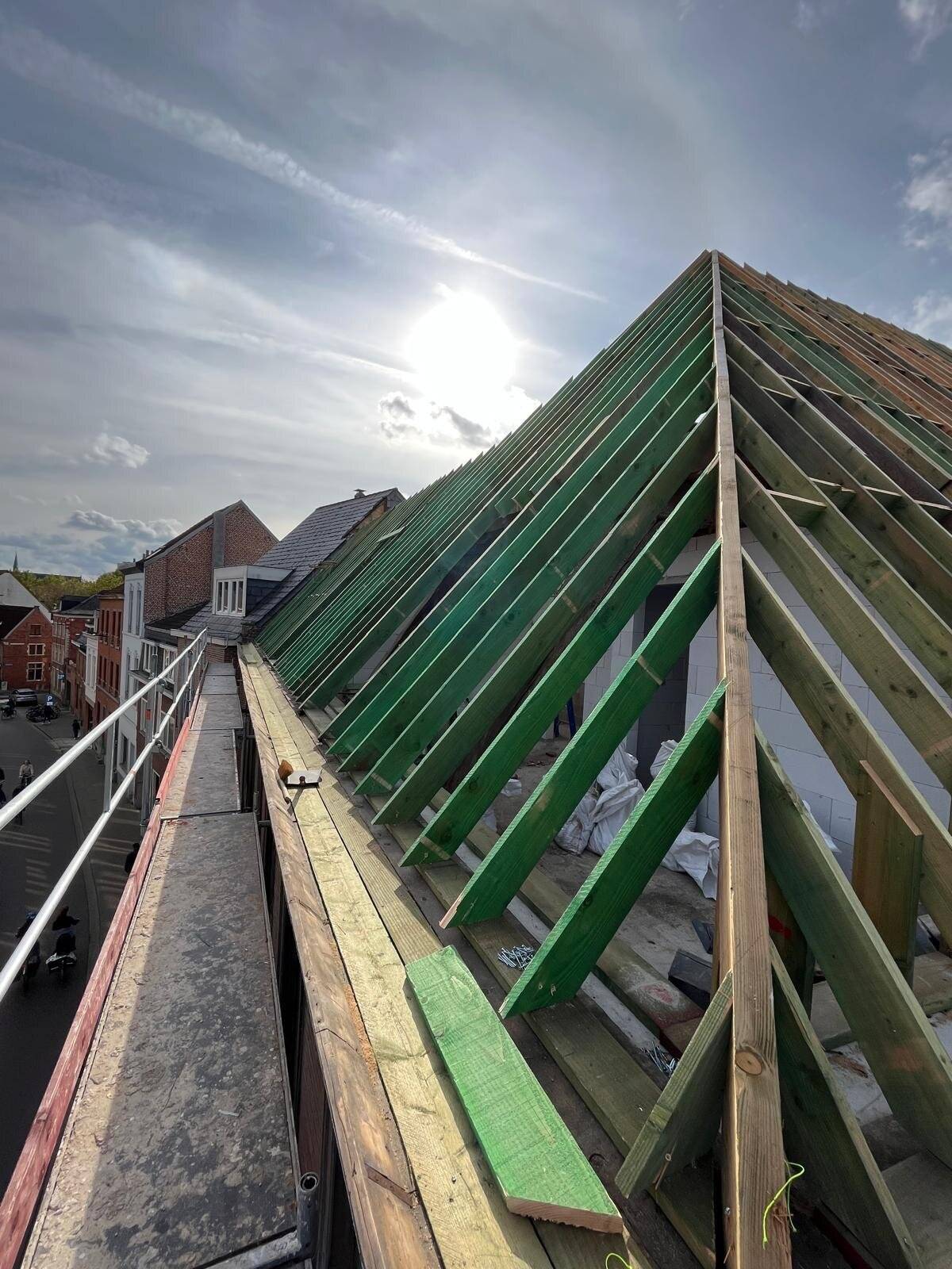 Zijaanzicht van een nieuw hellend dak in opbouw met houten spanten en deels geplaatste dakpannen.