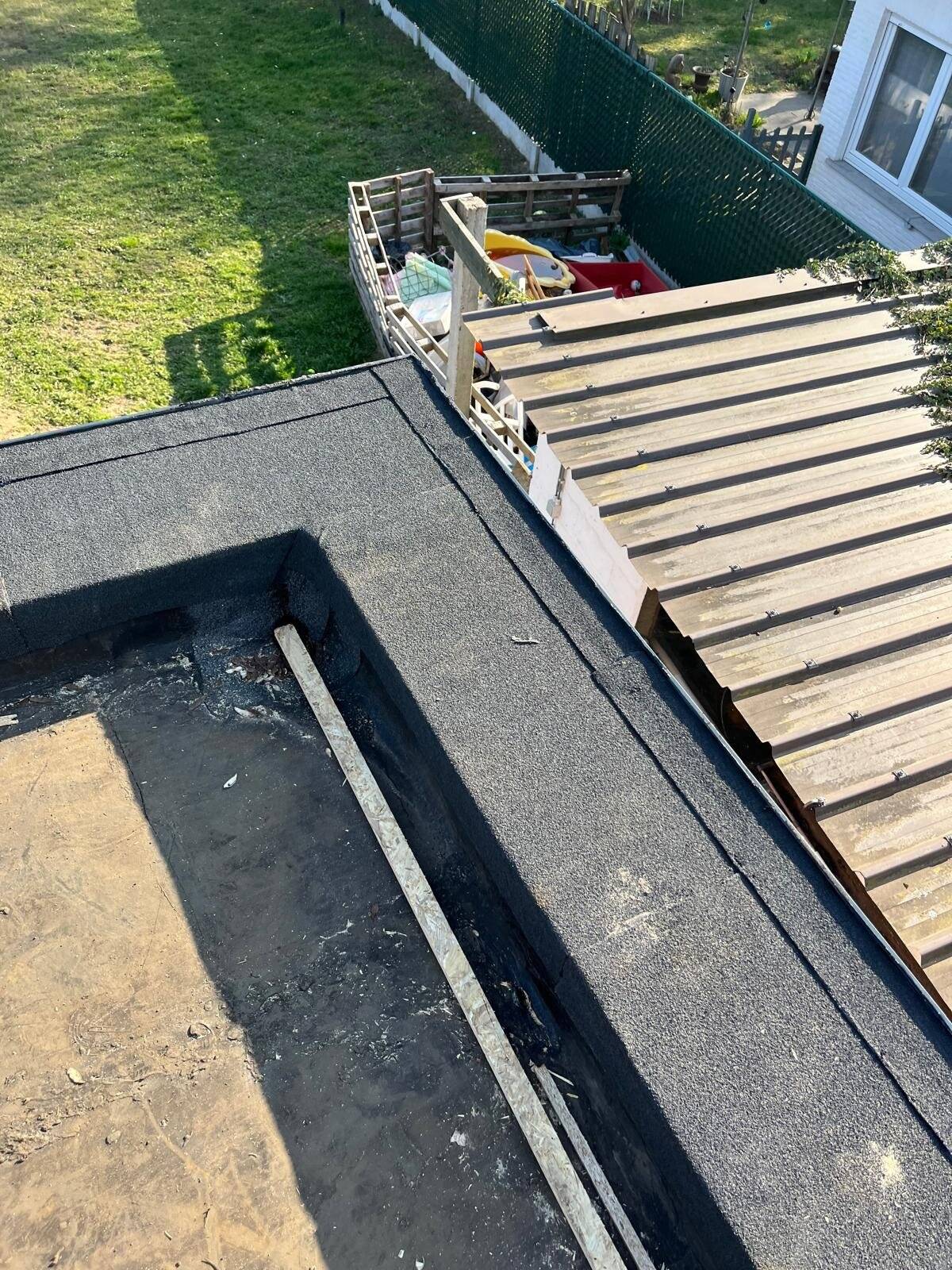 Detail van vernieuwd plat dak aan de rand van een gebouw, met een bouwwerf op de achtergrond.