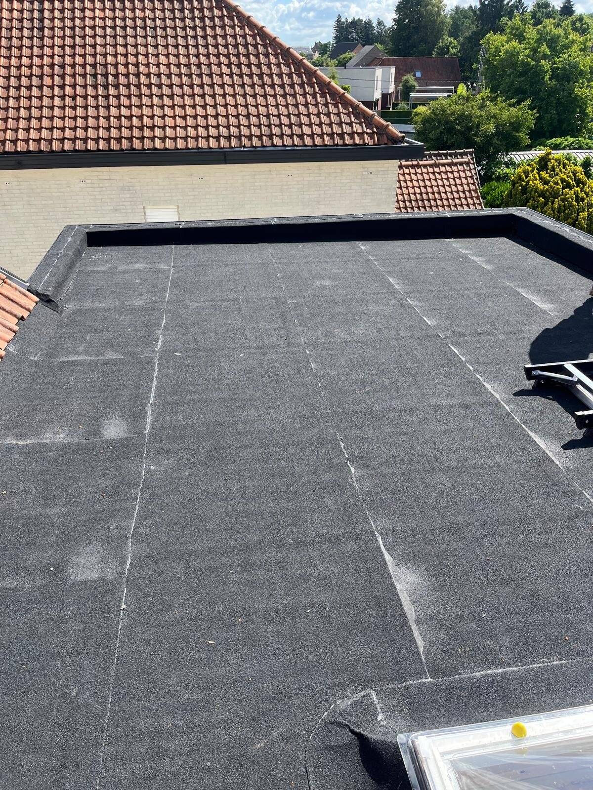 Nieuw aangelegd plat dak met bitumenbedekking en een dakrand.