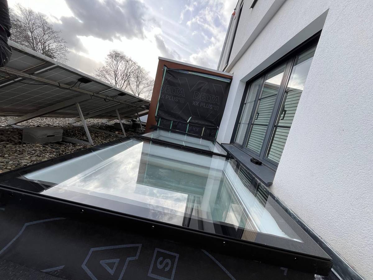 Nieuw geïnstalleerde daklichten op een plat dak van een modern huis met zonnepanelen in de achtergrond.