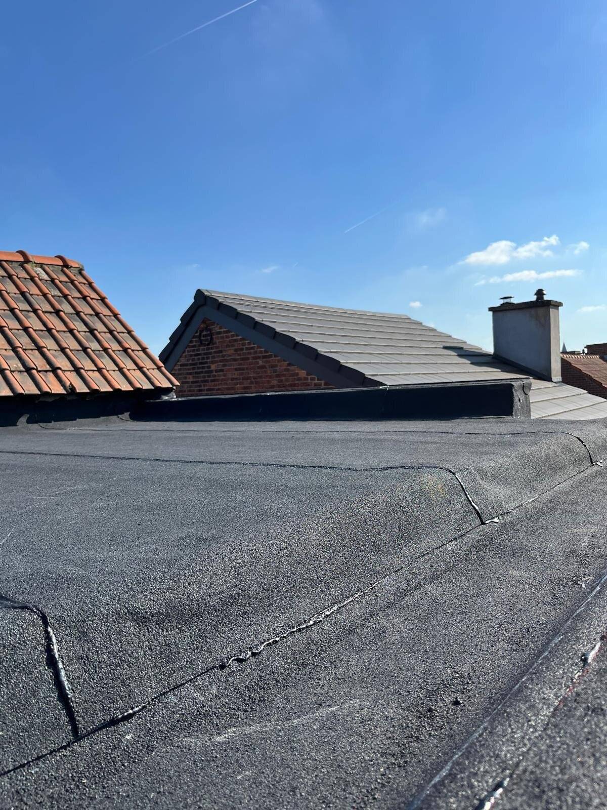 Combinatie van een plat dak en een hellend dak met pannen, gezien onder een blauwe lucht.