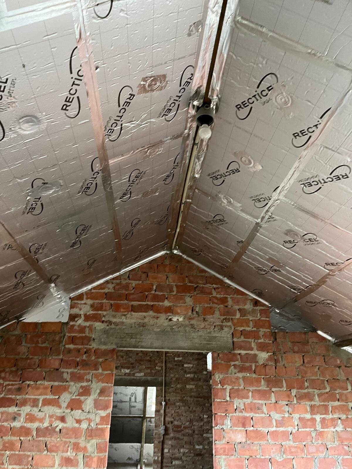 Geïsoleerd hellend dak met Recticel platen boven een gemetselde muur.