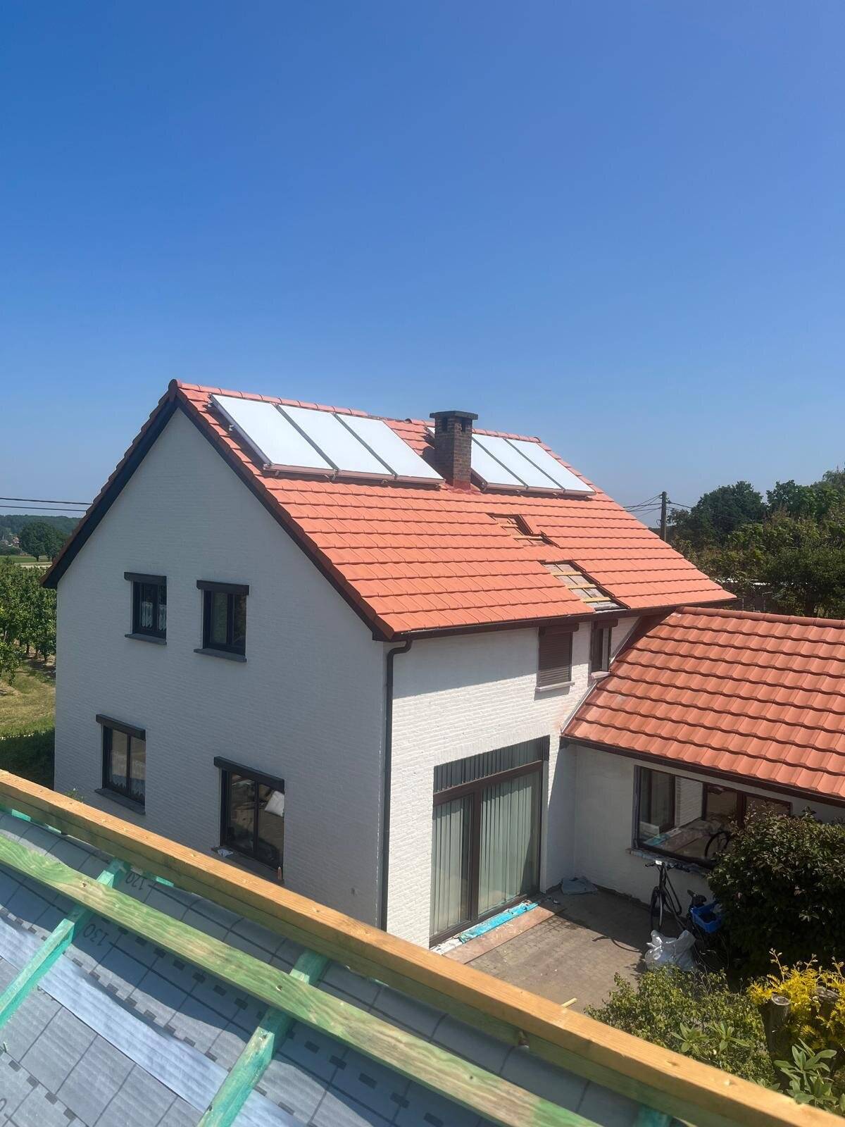 Huis met nieuw hellend dak, rode dakpannen en zonnepanelen, gezien vanaf een ander dak tijdens de werken.