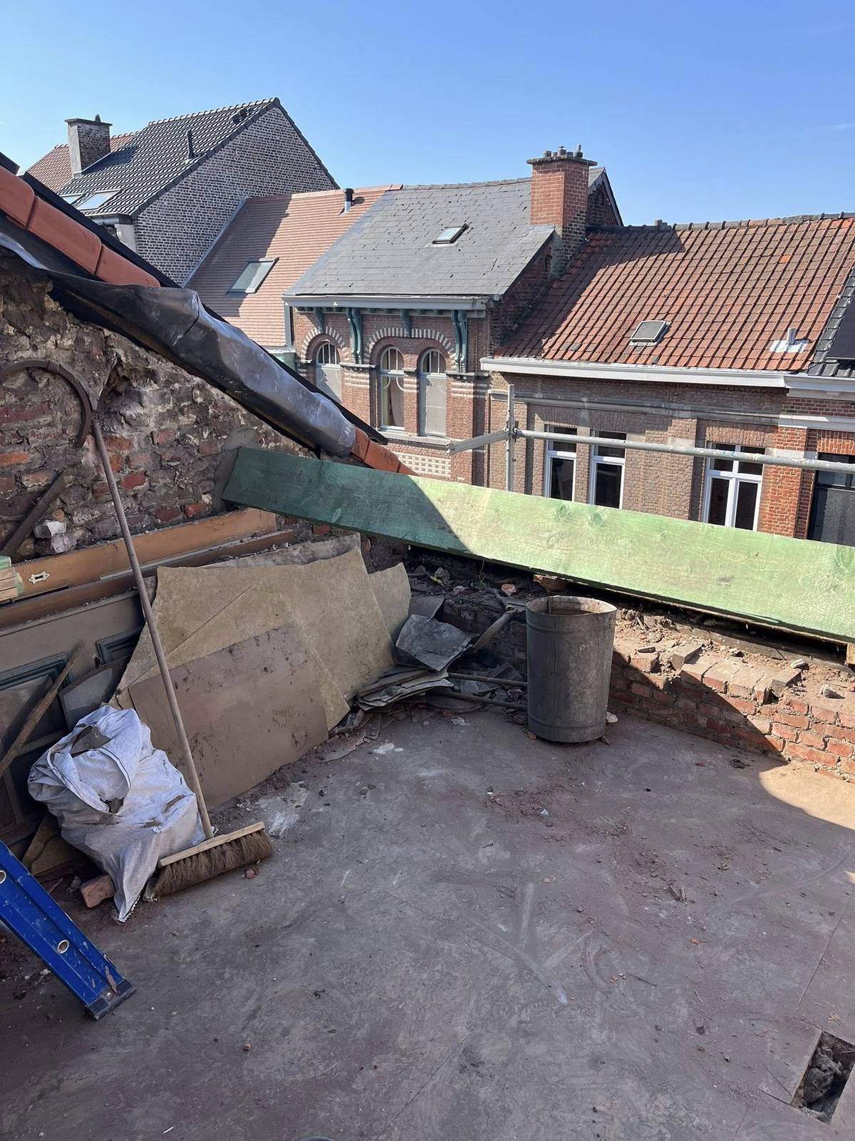 Werf op een plat dak met bouwafval en materialen, met omliggende huizen op de achtergrond.
